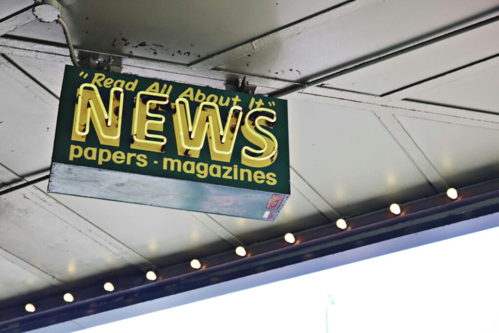 From below of illuminated signboard with news papers magazines inscriptions hanging on metal ceiling on street